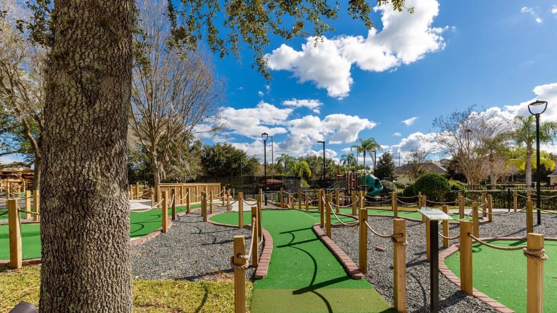 A miniature golf course with a green playing surface, wooden obstacles, and a clear sky.