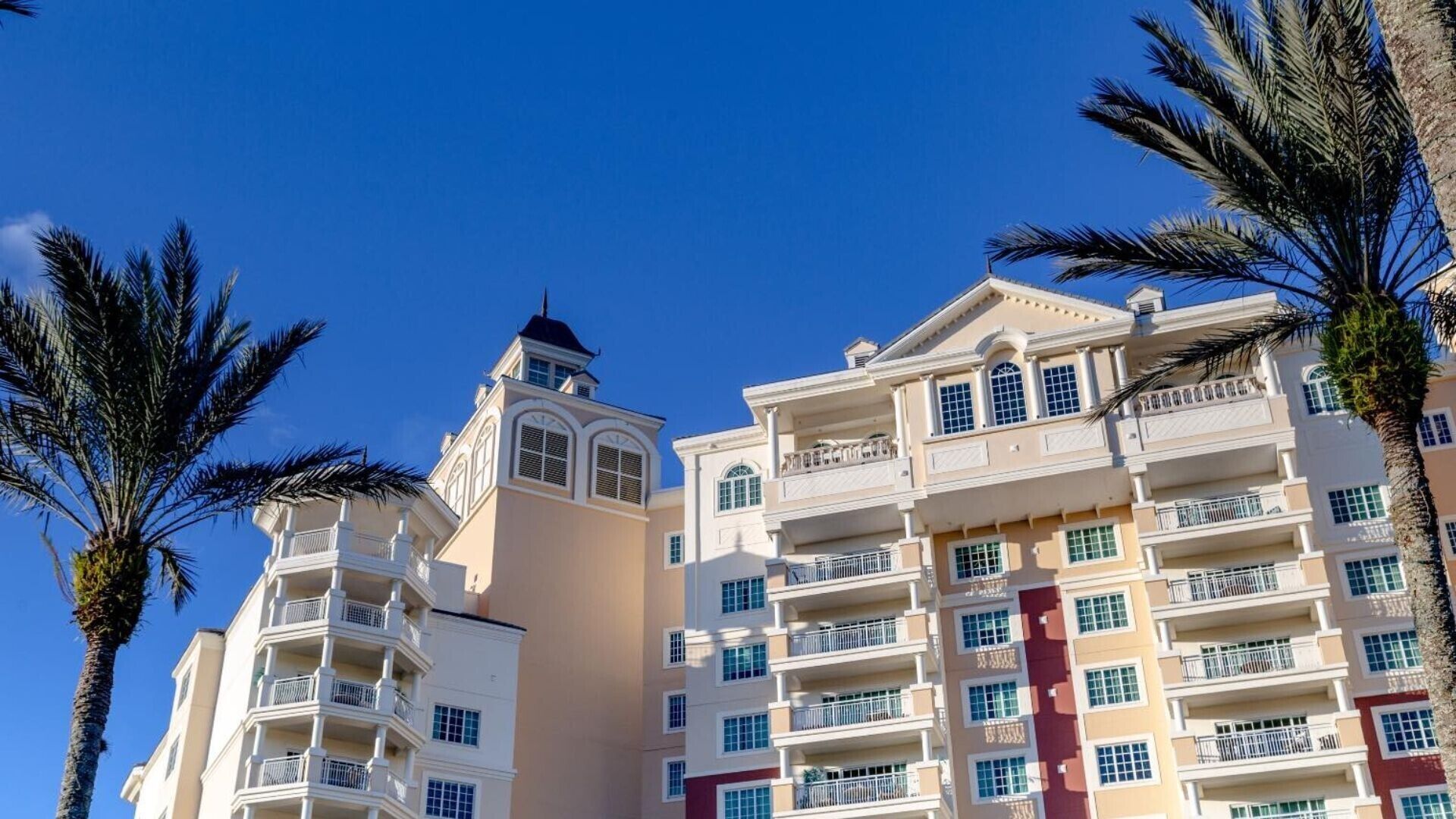 A multi-story hotel with balconies, a central tower, and palm trees.