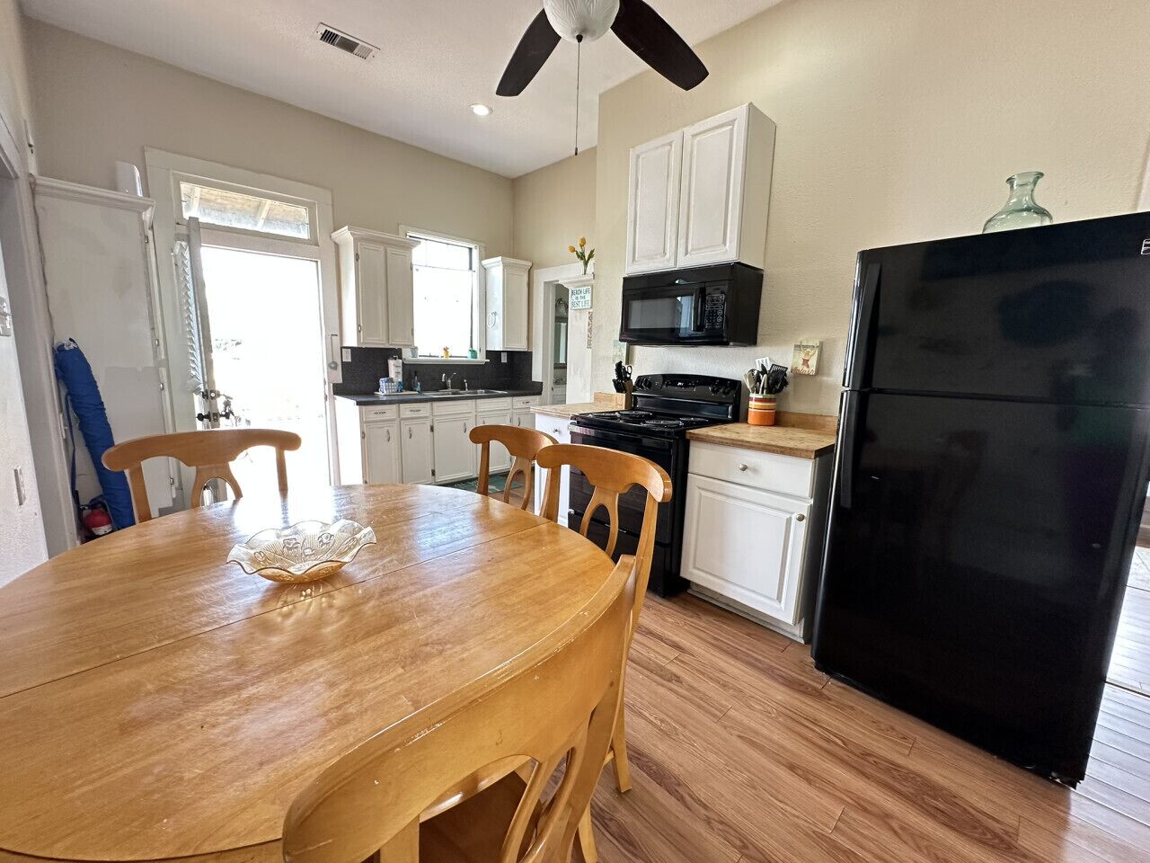 A kitchen with white cabinets, a black refrigerator, a wooden dining table, and a ceiling fan.