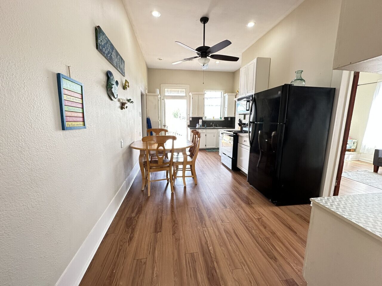 A kitchen with wooden flooring, a ceiling fan, and a black refrigerator.