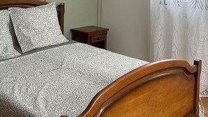 Ein Schlafzimmer mit einem hölzernen Bett, einem Nachttisch, einer Wandleuchte und einem Fenster mit Vorhang.