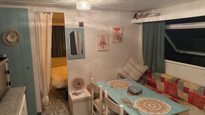 A compact room with a bed, a table with a decorative centerpiece, a mirror, and a window with curtains.