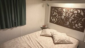Ein Schlafzimmer mit einem Bett, einem Kopfteil mit dekorativer Verkleidung, einem Fenster mit Vorhängen und einem Nachttisch mit Lampe.
