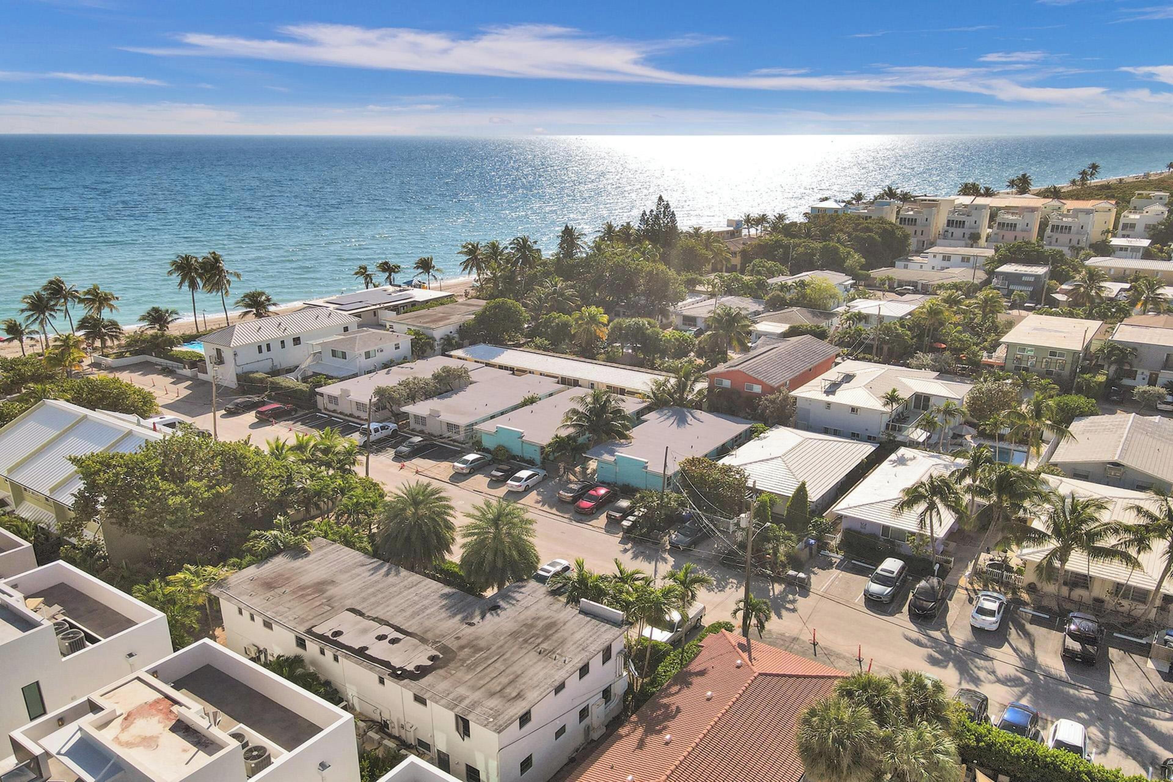 A coastal residential area with buildings, parked cars, and palm trees.