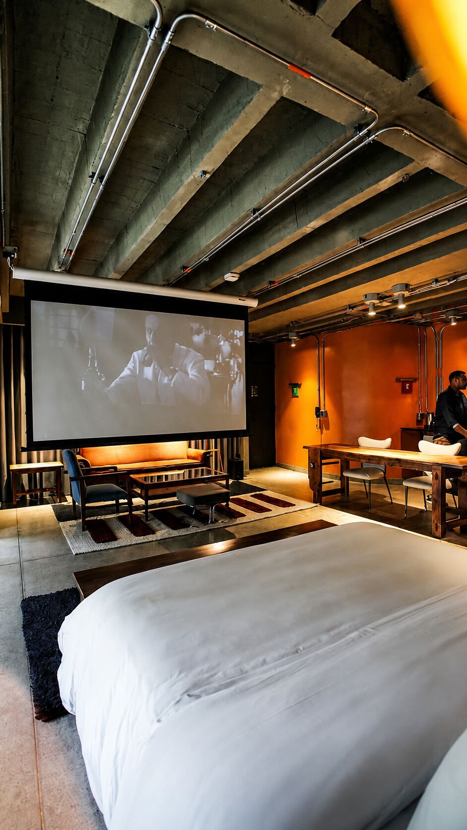 Une chambre moderne équipée d’un grand lit, d’un bureau et d’un écran de projection diffusant un film.