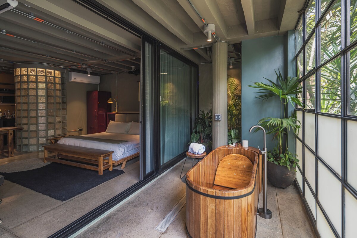 A modern hotel room with a large bed, a wooden bathtub, and a view through a glass door.