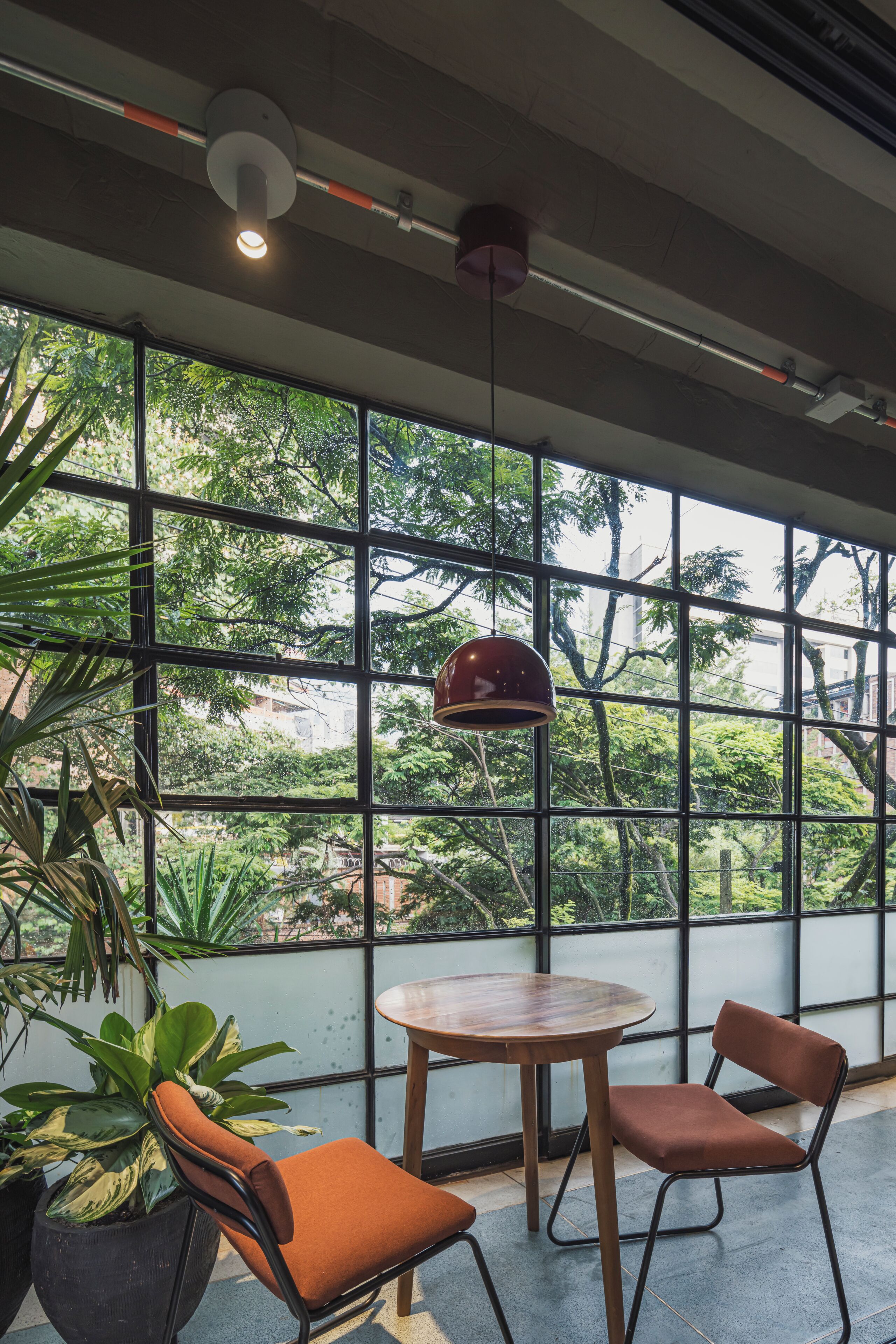 A room with large windows, a round table, two chairs, and a hanging pendant light.