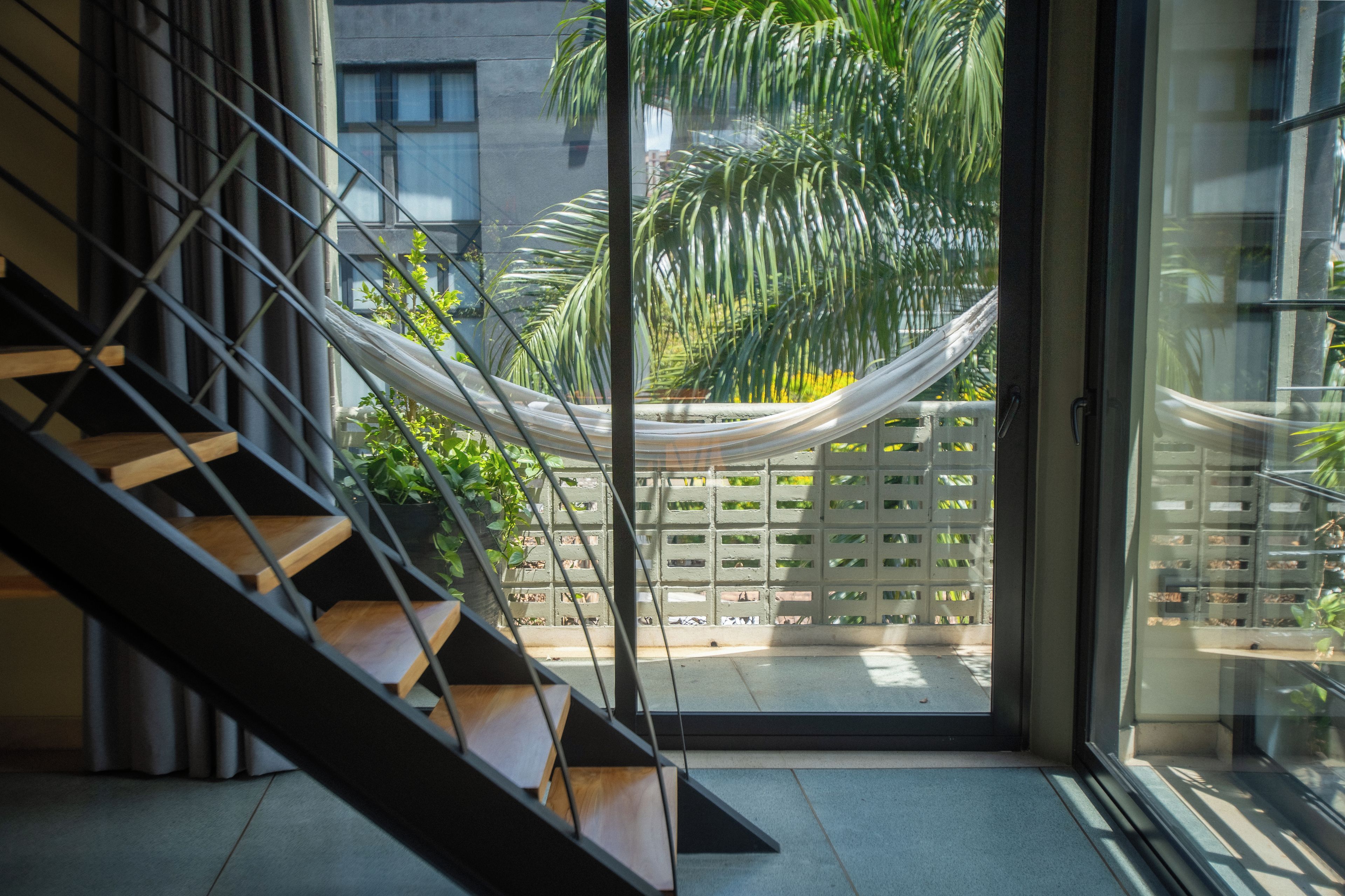 A modern interior with a staircase leading to a glass door opening to a balcony with a hammock and greenery.