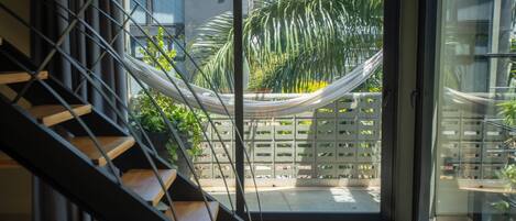 A modern interior with a staircase leading to a glass door opening to a balcony with a hammock and greenery.
