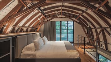 Dormitorio con techos altos, una cama grande, vigas de madera y vistas al exterior.