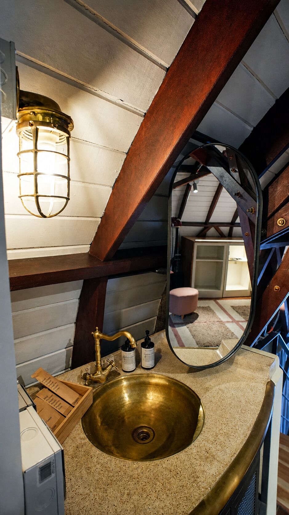 A bathroom with a brass sink, a mirror, and a hanging light fixture.
