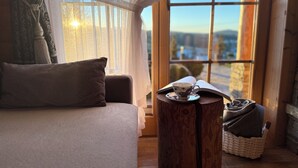 A cozy room with a sofa, a side table with a book, and a view through large windows. - Delightful 2-bedroom cottage in charming Ząb for your getaway (Ząb)