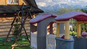 A wooden cabin with a play area featuring a slide and swings. - Delightful 2-bedroom cottage in charming Ząb for your getaway (Ząb)