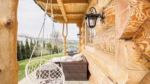 A log cabin interior with a hanging chair, wicker sofa, stone flooring, and a stone wall. - Delightful 2-bedroom cottage in charming Ząb for your getaway (Ząb)