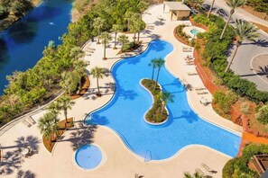 Ein Pool mit wellenförmigem Design, umgeben von Palmen und einem Strandbereich.