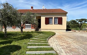 Ein Haus mit rotem Ziegeldach, einer Satellitenschüssel und einem steinernen Weg, der zum Eingang führt.
