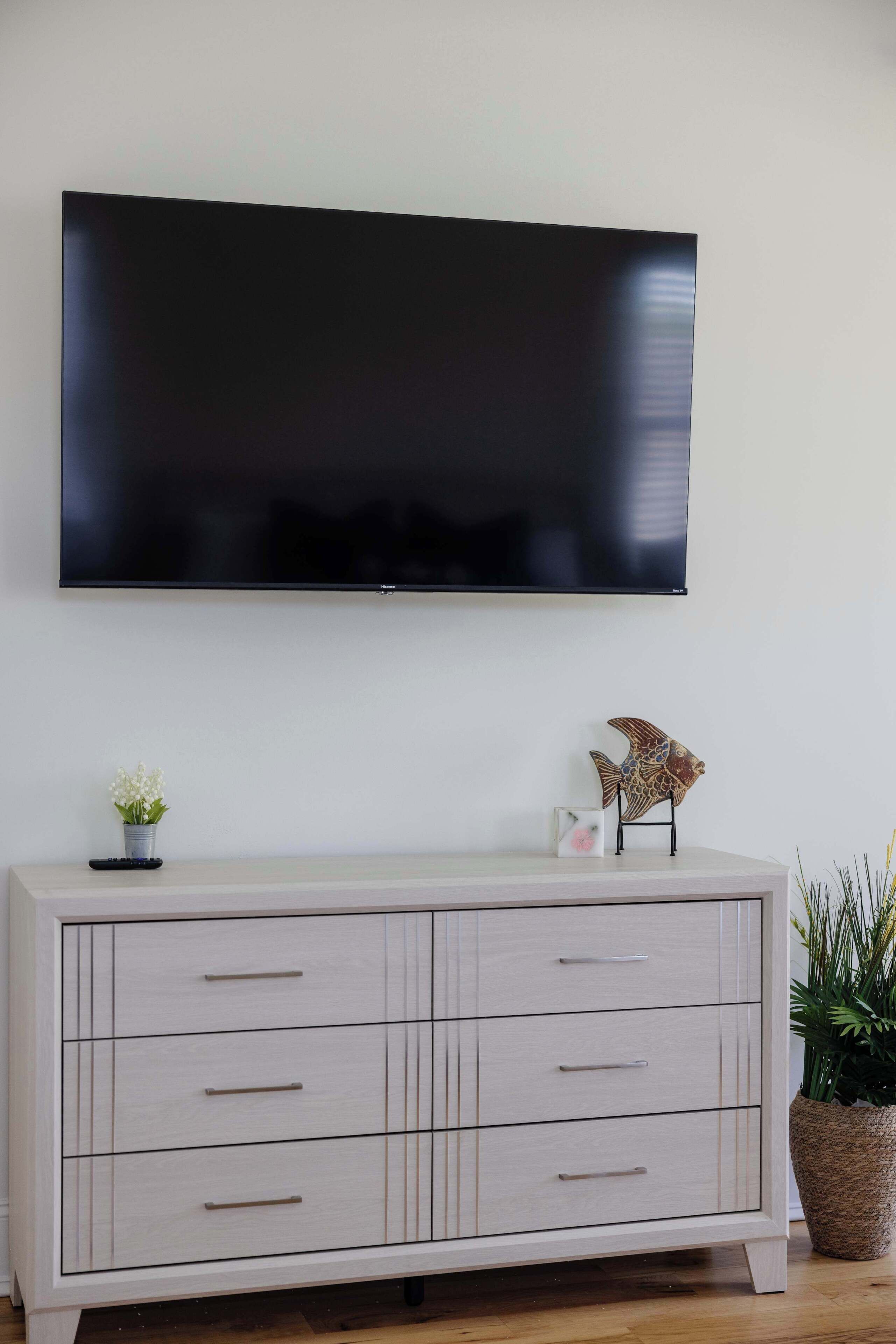 Een flatscreen-televisie bevestigd aan een muur boven een licht houten dressoir met lades.