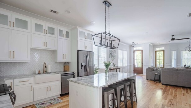 A modern kitchen with white cabinetry, a central island with bar stools, a stainless steel refrigerator, and a hanging light fixture. - Stunning Downtown 3BD-2.5BA Home| Near Forsyth Pk (Savannah)