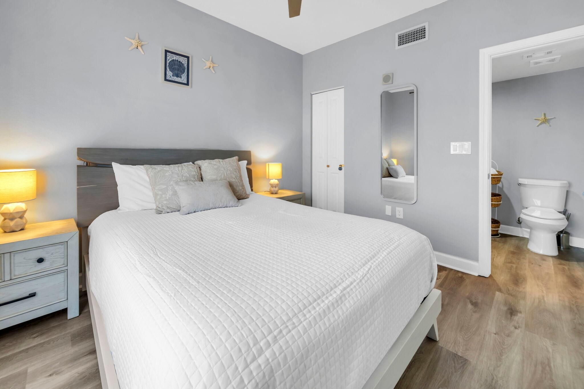A bedroom with a bed, bedside tables, a mirror, and a door leading to a bathroom.