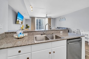 A modern kitchen with a double sink, granite countertop, white cabinets, and a built-in dishwasher. - Shores of Panama 925 (Panama City Beach)