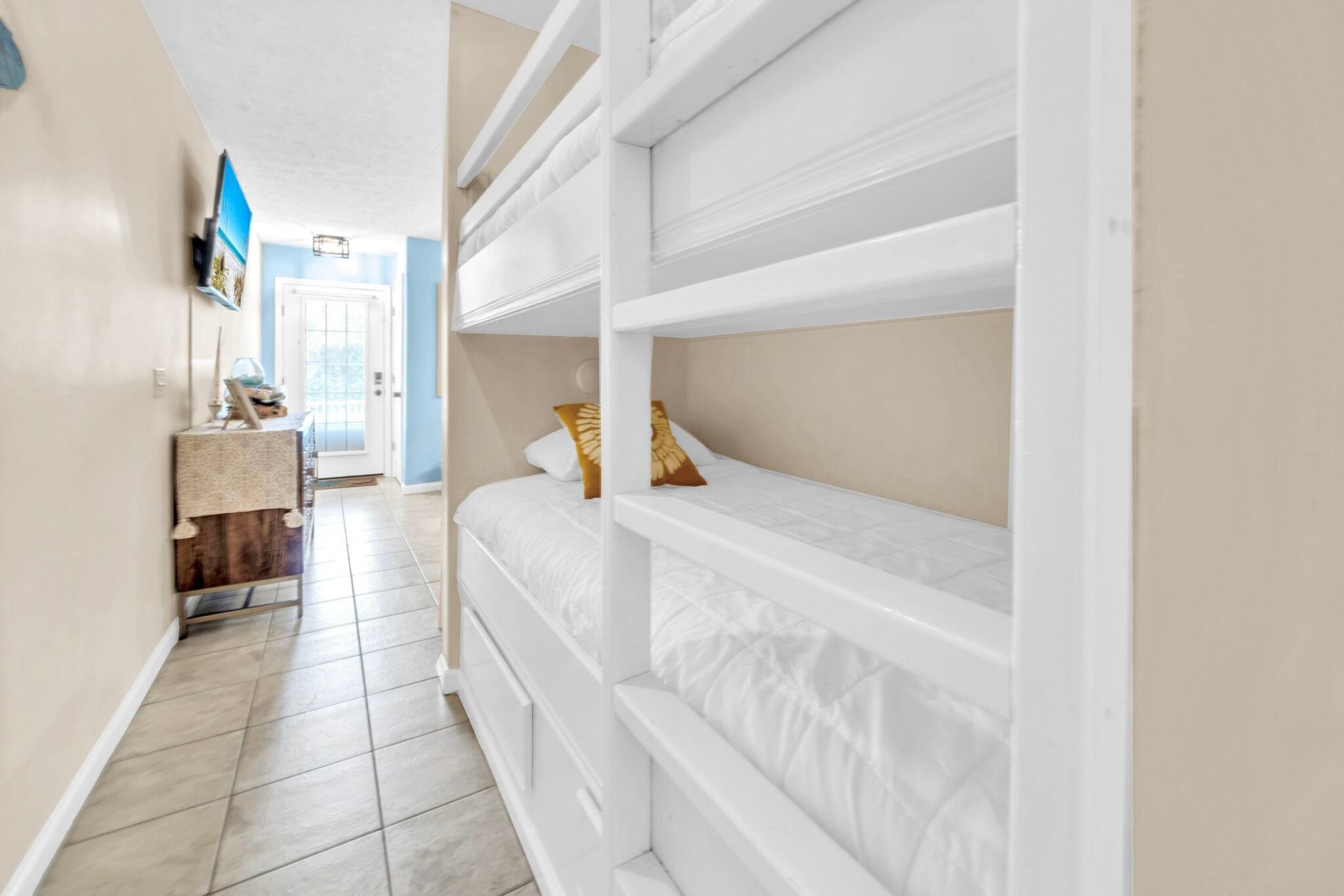 A narrow hallway with bunk beds, a small desk with a lamp, and a door leading to another room.