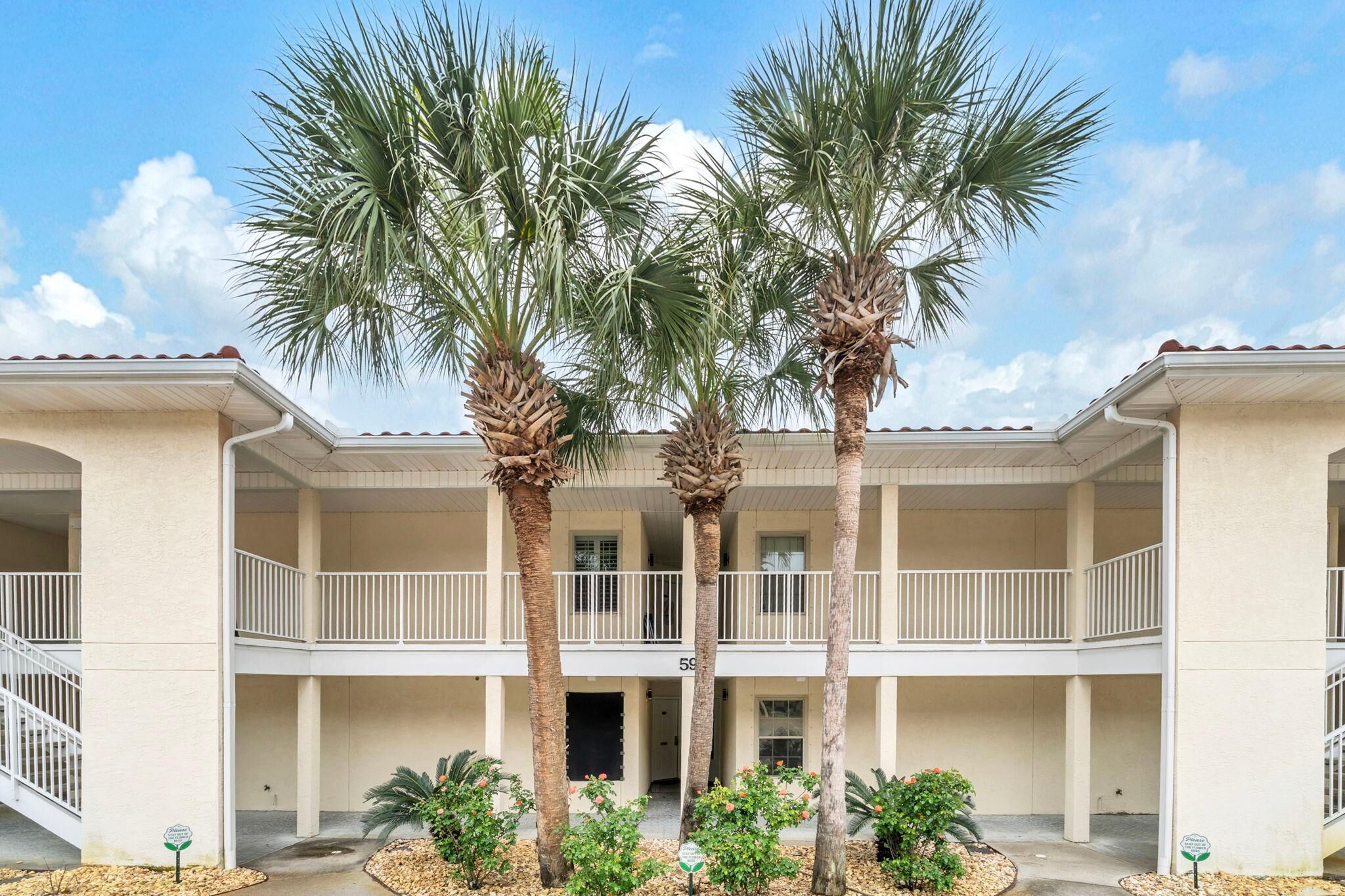 A multi-story building with a central courtyard, palm trees, and a balcony on the upper floor.