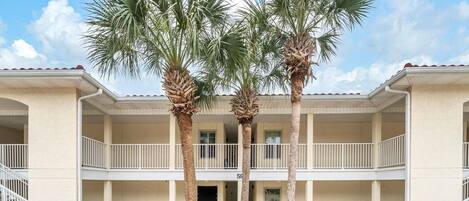 A multi-story building with a central courtyard, palm trees, and a balcony on the upper floor.
