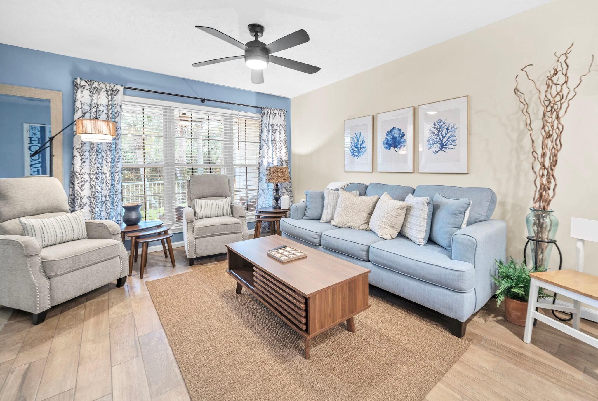 A living room with a sofa, armchairs, a coffee table, and a ceiling fan.