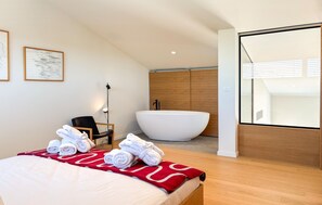 Ein modernes Hotelzimmer mit einem großen Bett, einer Badewanne und Blick auf die Stadt.
