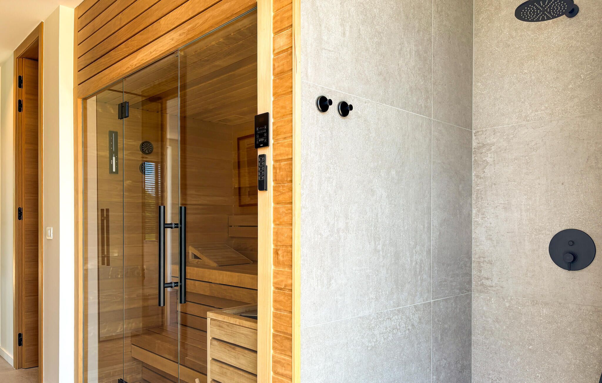 A modern sauna with glass doors, wooden panels, and a control panel.