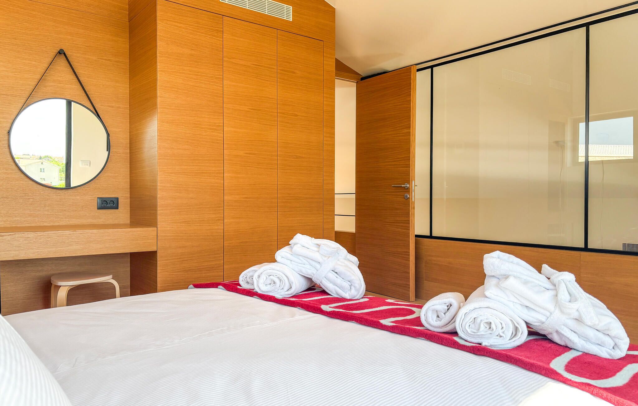 A hotel room with a bed, a mirror, a wardrobe, and a red towel mat.