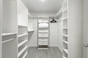 Un dressing ouvert avec des étagères, une tringle à vêtements et un meuble à tiroirs central.