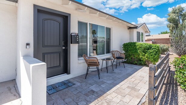 A house with a dark front door, a welcome mat, two wicker chairs, and a small table on a paved patio. - Minutes from Old Town Scottsdale with pool. Dual Primary BDRS. (Scottsdale)