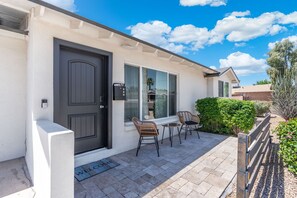 A house with a dark front door, a welcome mat, two wicker chairs, and a small table on a paved patio. - Heated Pool! Minutes from Old Town Scottsdale. Dual Primary BDRS. (Scottsdale)