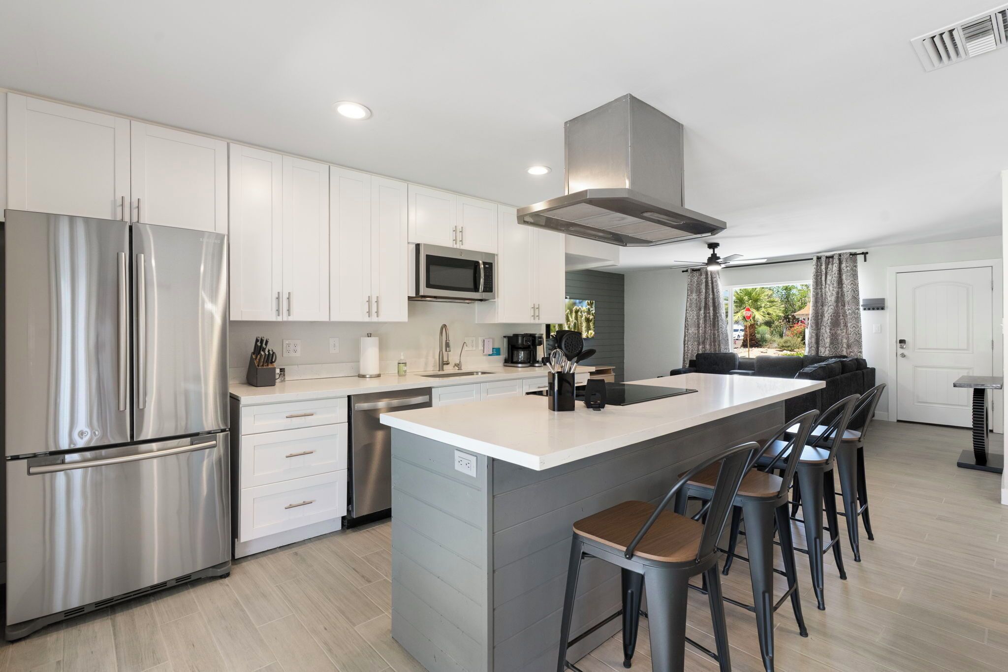 A modern kitchen with stainless steel appliances, a central island with bar stools, and a dining area with a sofa.