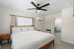 A bedroom with a bed, a ceiling fan, a nightstand, a window with curtains, an air conditioning unit, and a bathroom visible through an open door. - Minutes from Old Town Scottsdale with pool. Dual Primary BDRS. (Scottsdale)