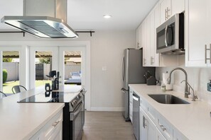 A modern kitchen with white cabinetry, stainless steel appliances, and a large island with a sink. - Minutes from Old Town Scottsdale with pool. Dual Primary BDRS. (Scottsdale)