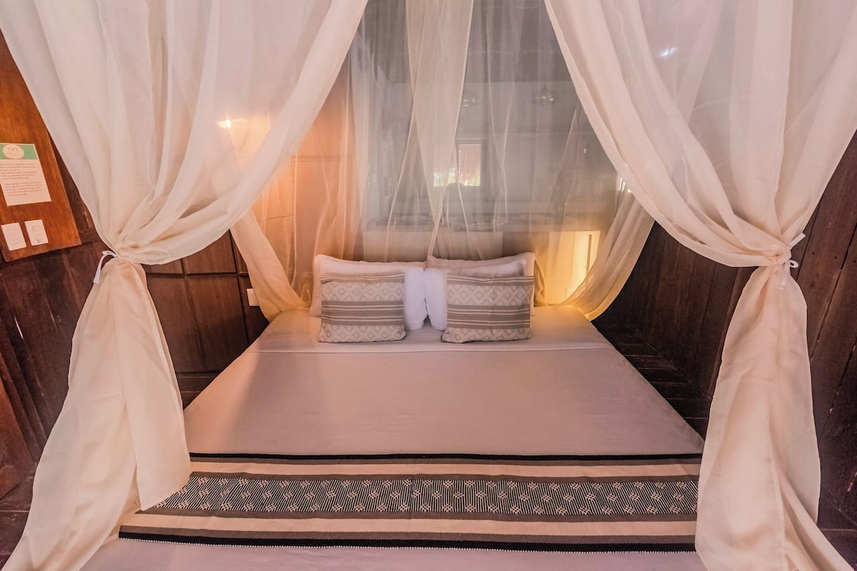 Una cama con dosel, un tapete estampado y una pared de madera.