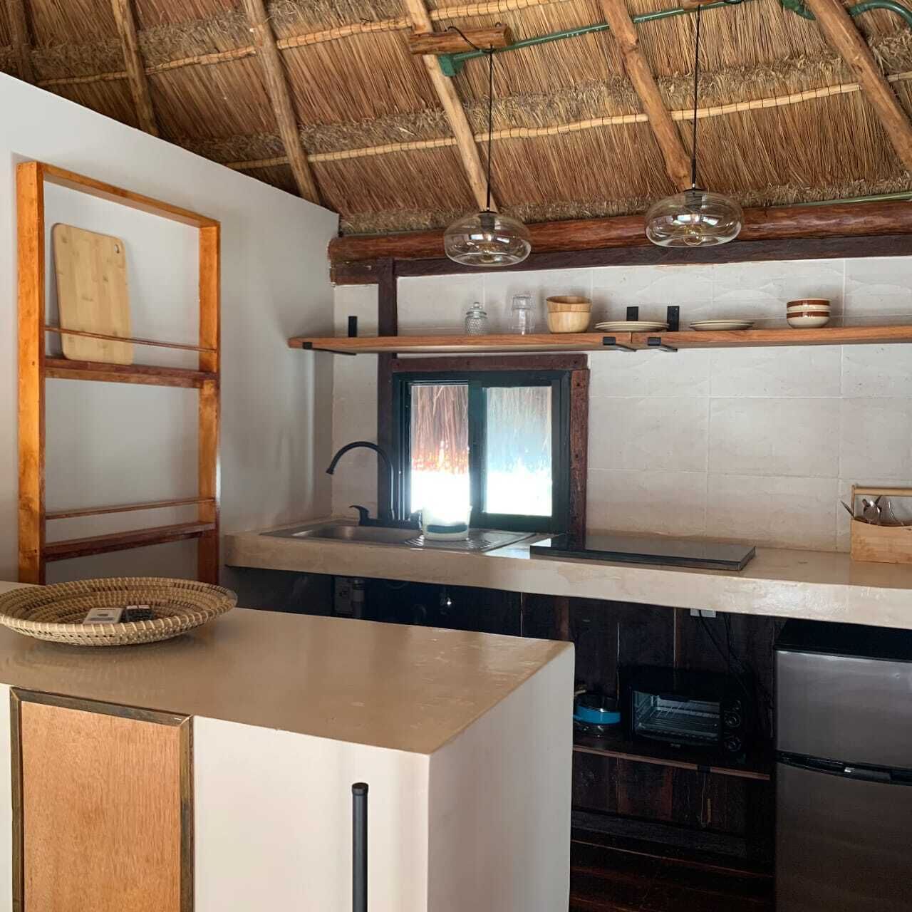 Una cocina con techo de paja, una escalera de madera, un lámpara colgante y un horno empotrado.