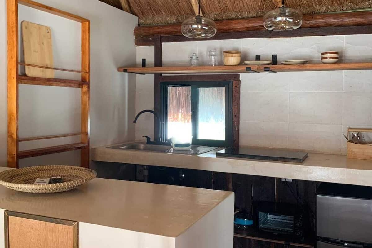 Una cocina con techo de paja, una escalera de madera, un lámpara colgante y un horno empotrado.