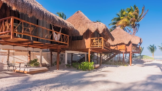 Des bungalows sur pilotis dotés de toits de chaume, de balustrades en bois et bordés par une plage de sable.