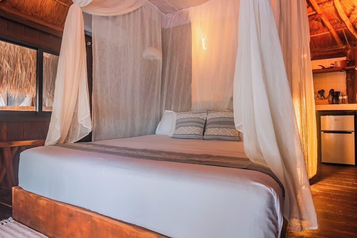 Una cama con dosel, cabecera de madera y mesita de noche con lámpara.