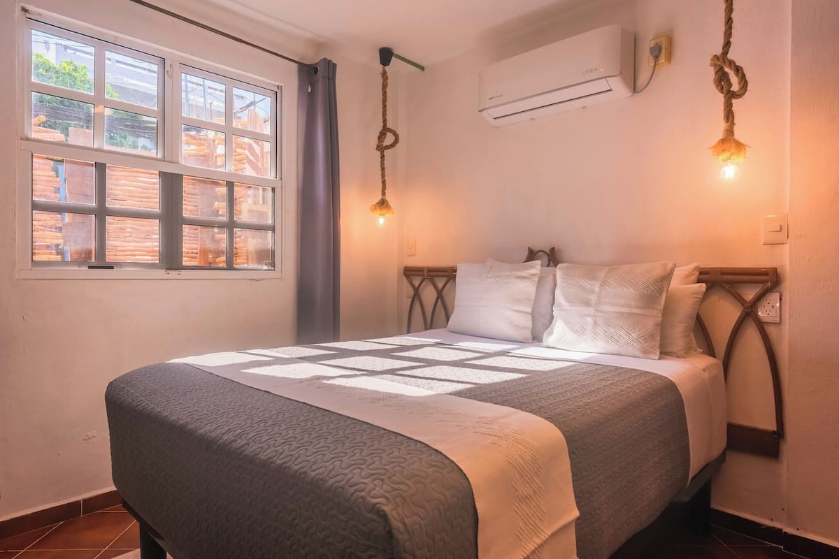 Un dormitorio con cama, ventana, aire acondicionado y lámpara colgante.