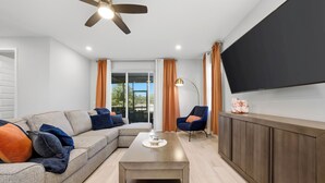 Ein modernes Wohnzimmer mit einem Ecksofa, einem Couchtisch, einem an der Wand montierten Fernseher und einem Deckenventilator.