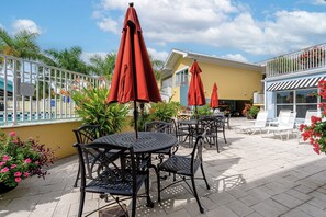 Terras met tafels en stoelen, rode parasols en een zwembad op de achtergrond.