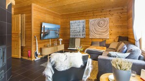 A cozy cabin interior with a wooden ceiling, a television, a sofa, a chair, and a fireplace. - Mökki maui by Interhome (Pelkosenniemi)