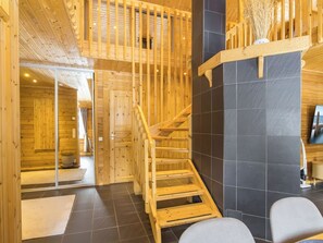 Un intérieur en bois avec un escalier, une vue sur une pièce où se trouve un lit, et un tableau accroché au mur.
