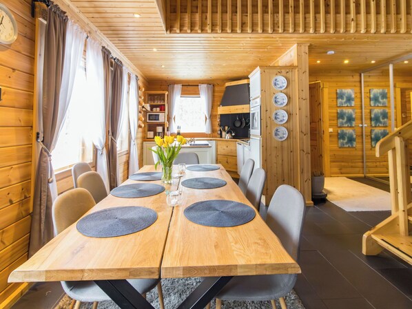 A wooden interior with a dining table set for four, a kitchen area, and a staircase.