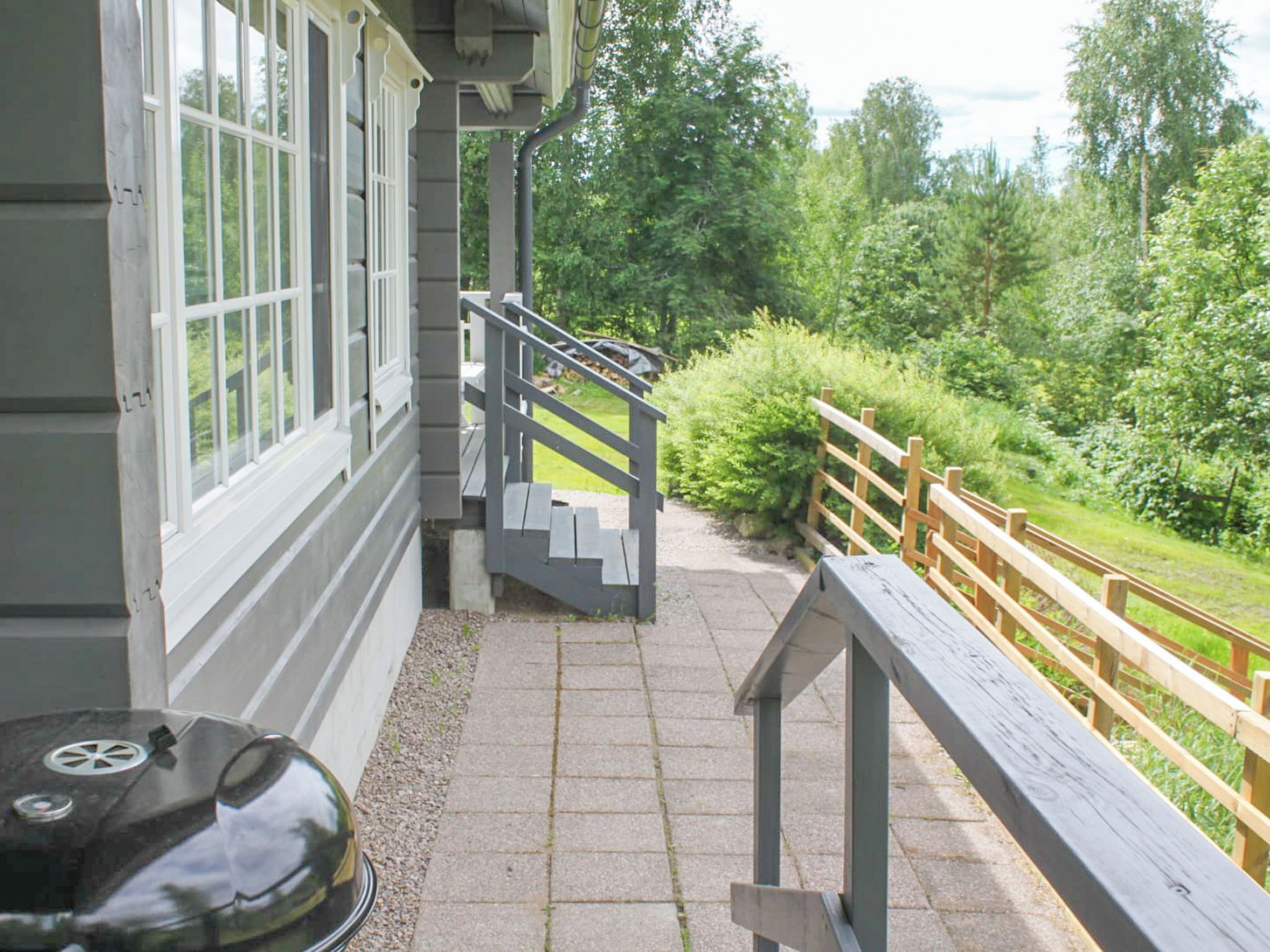 Une terrasse en bois dotée d’une rambarde, d’un barbecue et d’un escalier menant à un bâtiment aux grandes fenêtres.