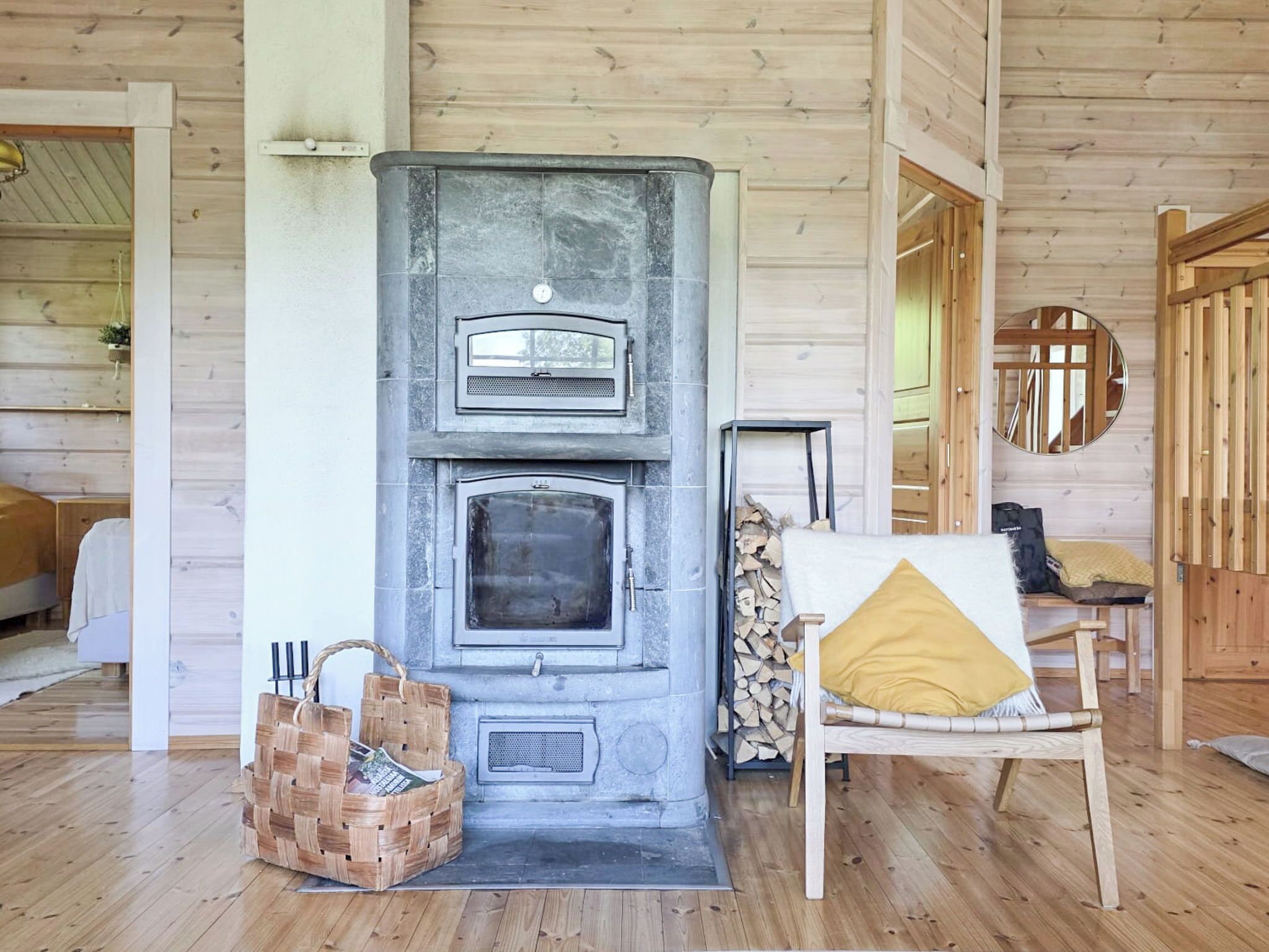 Interior de uma cabana de madeira com lareira de pedra, cesta de palha e cama de madeira.